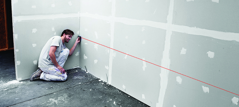 A worker uses a Bosch 65 foot laser measure on drywall.
