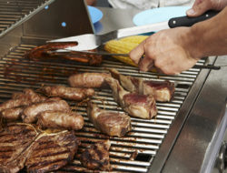 A man grills a variety of meats on a grill.