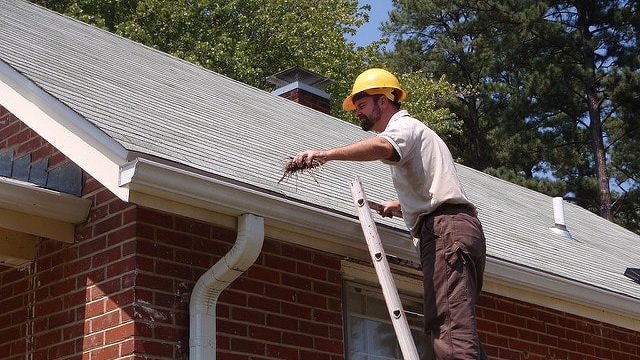 man safely cleaning gutter from a ladder