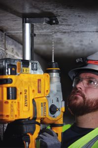 Construction worker using a DEWALT hammer drill to drill a hold in concrete overhead.