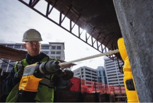 Construction worker drilling a hole in a concrete wall using a dewalt drill and drill bit.