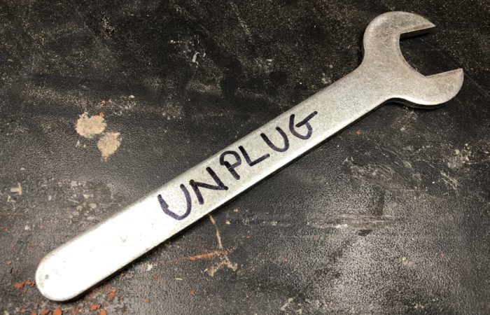 Router collet wrench lying on a black table top with the word "UNPLUG" written on it. This is a safety precaution that should be followed before working on a tool or changing a bit.