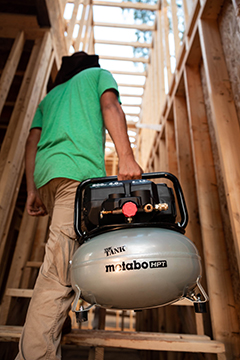 A worker carries The Tank pancake compressor up a flight of stairs.