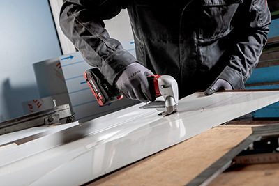 A metalworker cuts a sheet of metal using the Metabo 18 Volt Cordless Shear.