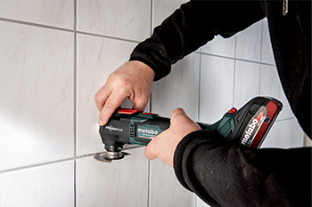 A Metabo MT 18 LTX BL QSL Cordless Multi-tool is used to clean out grout between tile.
