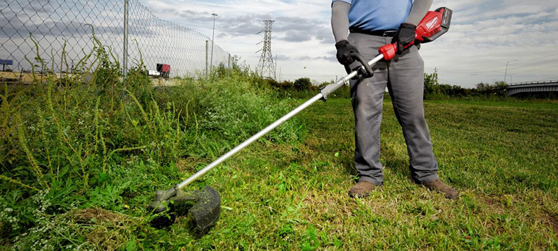 A worker cuts some brush with the Milwaukee M18 FUEL QUIK-LOK Cordless String Trimmer.