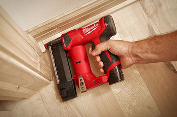 A worker attaches baseboard trim using an Milwaukee M12 23-Gauge Cordless Pin Nailer.