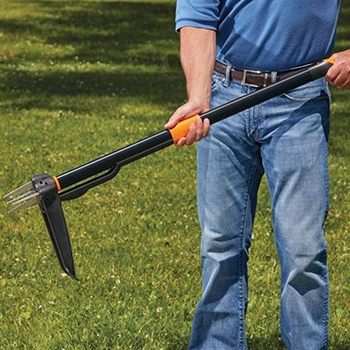 A man releases a weed using the easy-eject mechanism on a Fiskars stand-up 4-claw weeder.