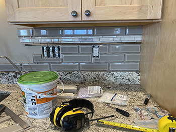 Tools litter a counter while a backsplash is installed.