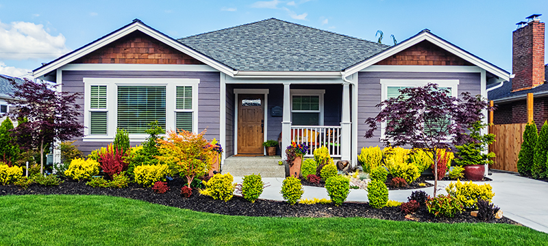 A front yard with beautiful landscaping, such as bushes, flowers, plants, and mulch surrounded by plastic edging.