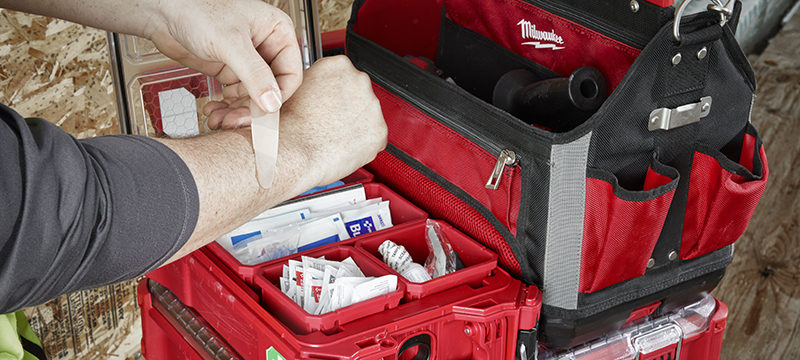 A worker applies a bandage from the Milwaukee PACKOUT 76-Piece First Aid Kit.