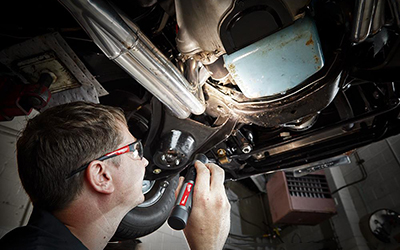 A mechanic uses a Milwaukee USB Rechargeable Flashlight to look under an engine.