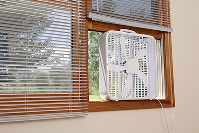 A box fan sits in an open window, creating a cross breeze.