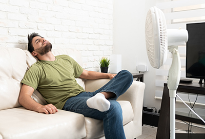 A man relaxes on a couch in front of a fan.