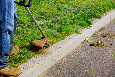 A string trimmer is used along the edge of a curb.