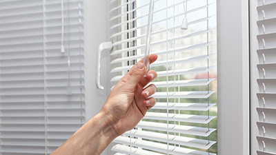 A woman closes the blinds on a window.