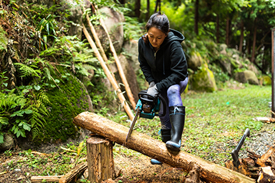 A woman uses a chainsaw to cut a downed tree.