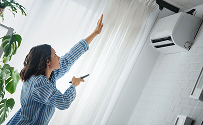 A woman uses a remote to control the temperature of her wall AC unit.