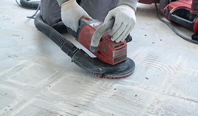 A concrete grinder is used to remove old glue from a floor.