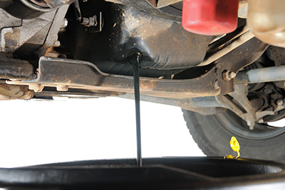 Oil is drained underneath a vehicle into a drip pan.