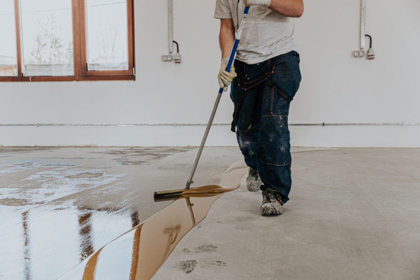A squeegee is used to spread epoxy on a garage floor.