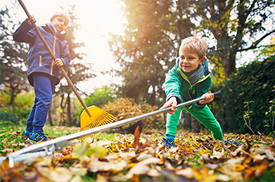 Two kids rake leaves during a fall day.
