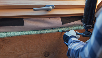 Canned spray foam is used to fill a gap under a window.