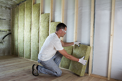 A man installs fiberglass insulation between wall studs.