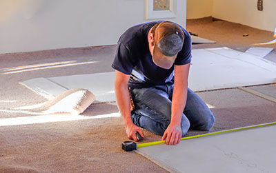 Young man carpenter measuring new rugs he's going to install in house; sunlight coming from the windows