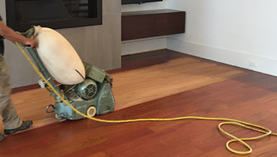 A worker sands a hardwood floor.