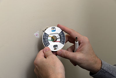 Close-up of Hand installing wires and mounting plate for modern round thermostat for air conditioning unit in a house
