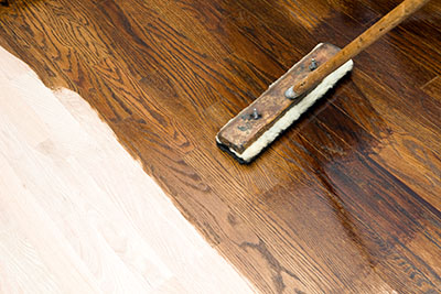 A staining sponge is used to apply stain to a wood floor.
