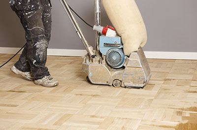 A drum sander is used to strip stain off a hardwood floor.
