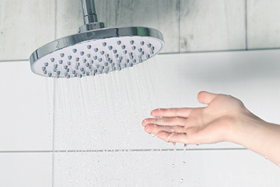 A hand tests the temperature of water from a shower head.