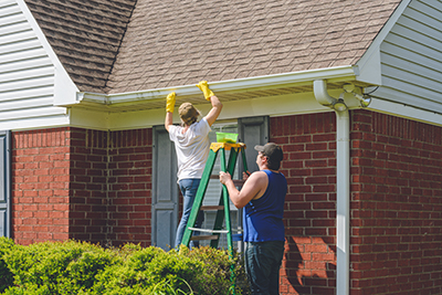 Woman Cleaning Gutters While Standing On Ladder