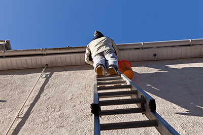 Tradesman climbing a ladder to clean and unblock the gutters and pipes