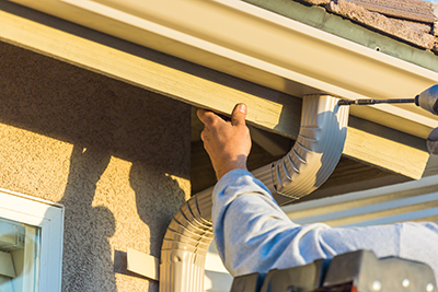 Worker Attaching Aluminum Rain Gutter and Down Spout to Fascia of House.Worker Attaching Aluminum Rain Gutter to Fascia of House.