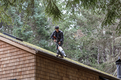 Man cleaning rain gutters on roof with blower