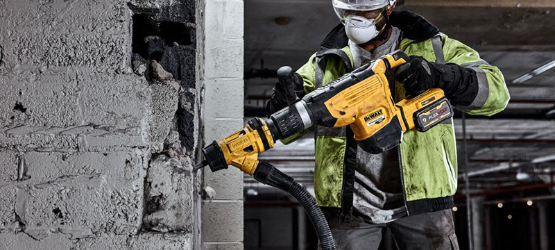 A construction worker uses a DEWALT 60V MAX Chipping Hammer to break down a concrete wall.