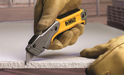 A DEWALT standard utility knife cuts through a piece of drywall.