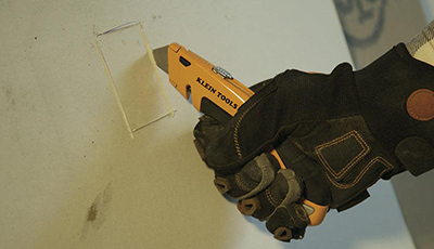 A Klein Tools retractable utility knife is used to cut a piece of drywall.