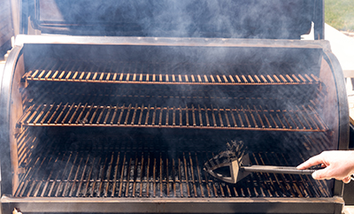 A pellet grill is cleaned with a grill brush.