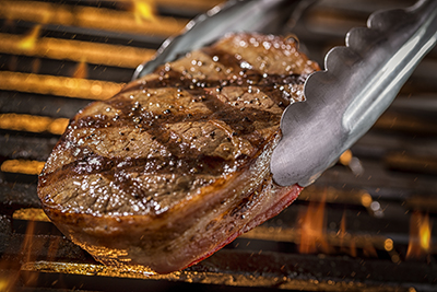 Tongs are used to flip a filet mignon steak on a grill.