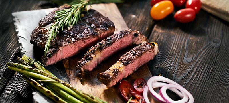 A medium rare ribeye steak on a board with thyme and asparagus.