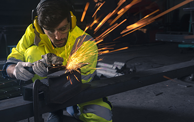 A worker properly using an angle grinder on a piece of metal.