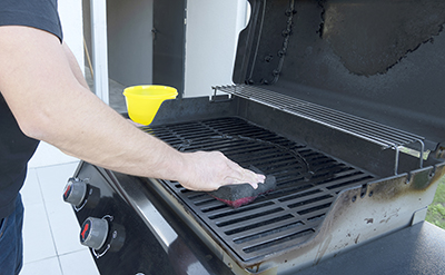 A soft scrubber is used to clean a gas grill grate.