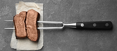 Two pieces of well-done steak on a fork.