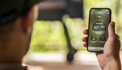 A man checks the temperature of his Traeger grill on their app using WiFIRE technology.