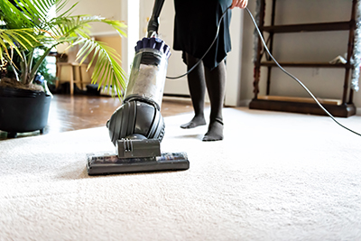 A bagless vacuum is used to clean carpet in a living room.