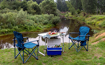 Camp chairs at a picnic table by a riverside.